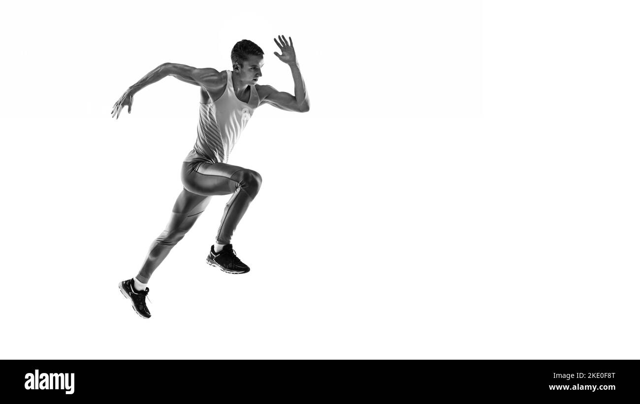 Black and white portrait of muscular male athlete, runner, jogger in motion isolated on white background. Monochrome. Sport, beauty, power and style Stock Photo