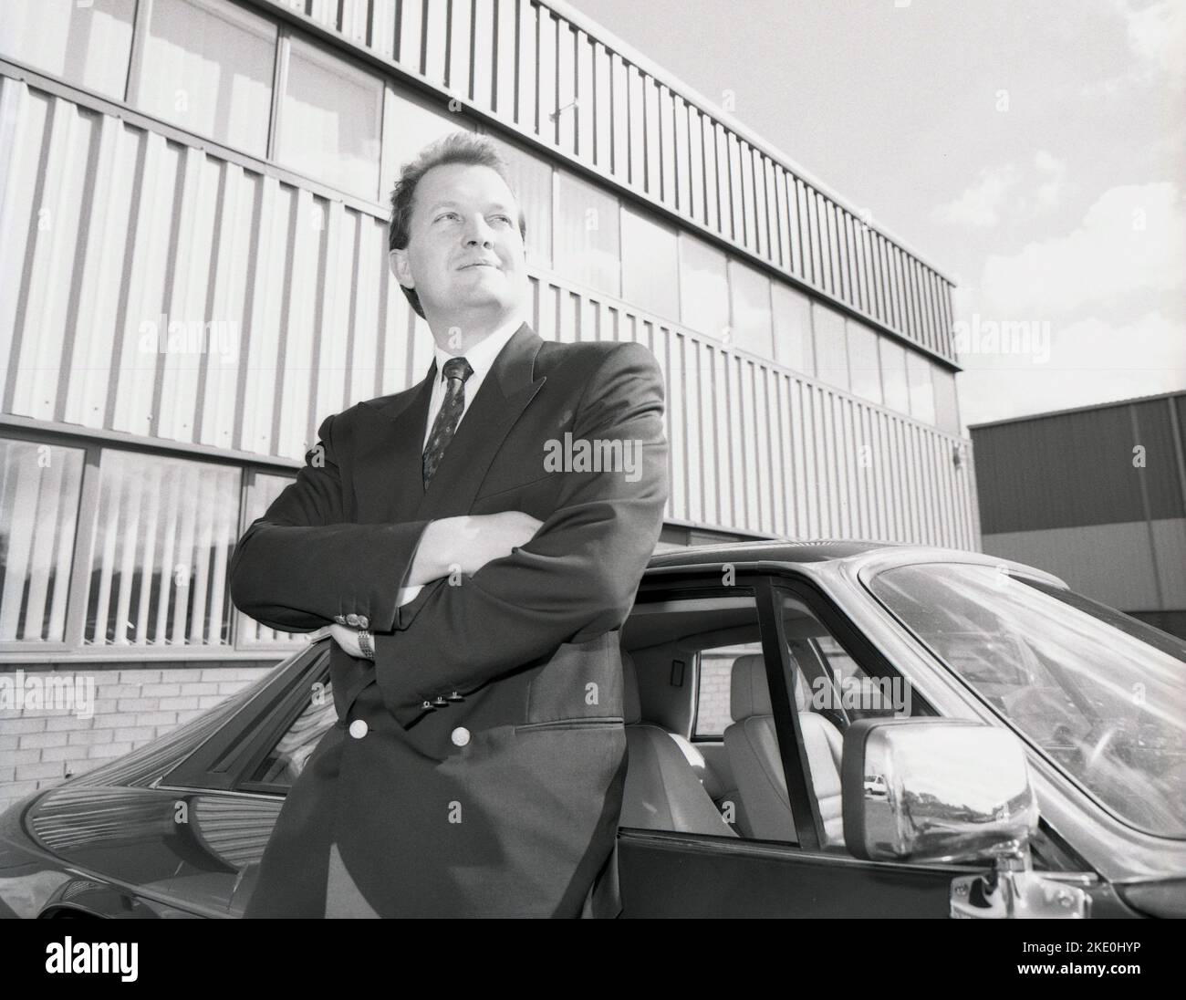 1980s, historiccal, successful business executive standing by his Jaguar sports car outside his offices, England, UK. Stock Photo