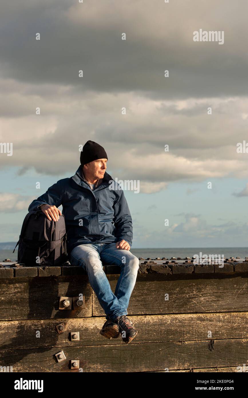 Guy with a backpack sitting resting enjoying the view after walking. Wearing outdoor clothes