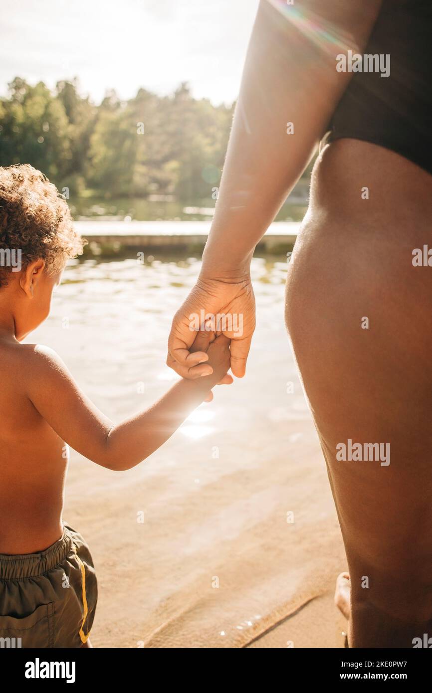 Woman holding hand of son while standing near lake on sunny day Stock Photo
