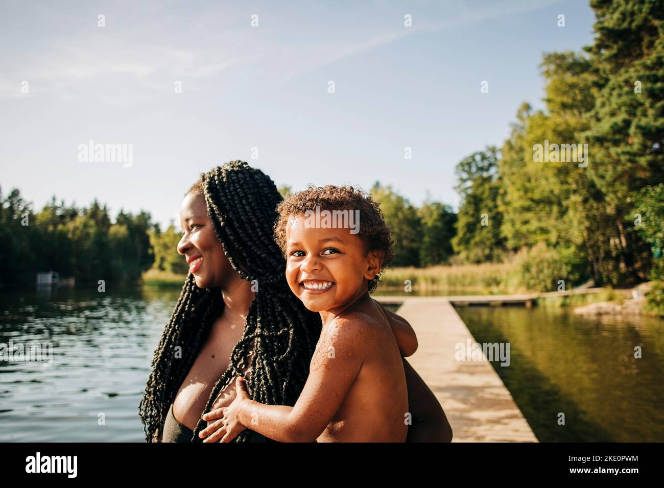Smiling woman carrying excited son at lake during vacation Stock Photo