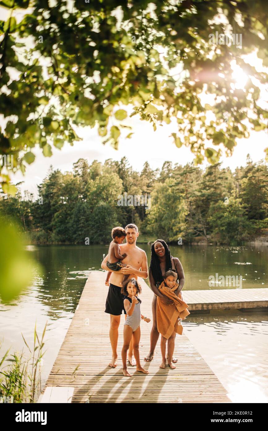 Happy family standing together on jetty at lake during vacation Stock Photo