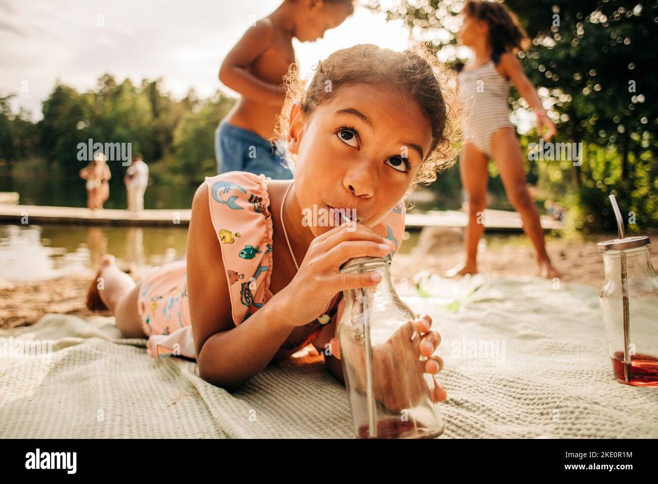 Girl looking away while drinking juice from bottle lying down on picnic