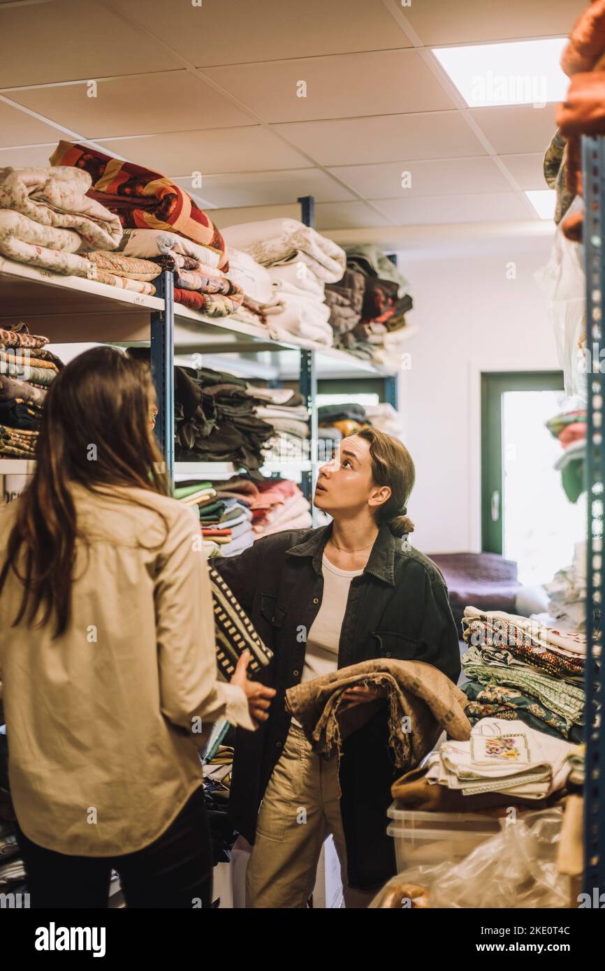 Female fashion designers talking while standing near rack at workshop Stock Photo