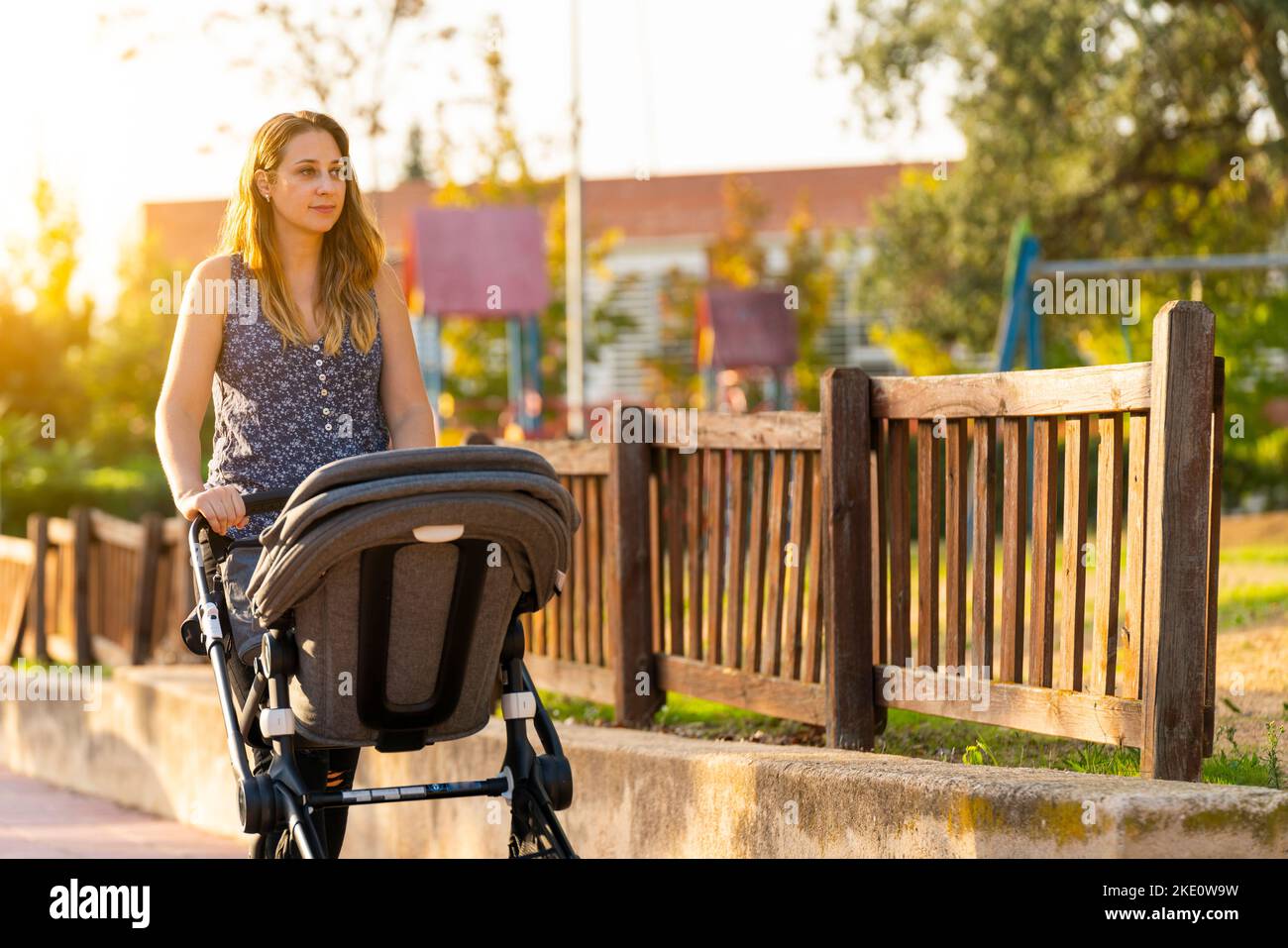 Mother and son walking with the baby stroller near the park Stock Photo