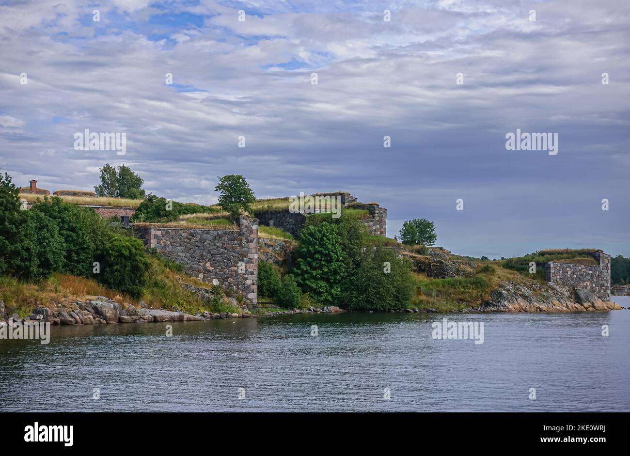 Helsinki, Finland - July 19, 2022: Suomenlinna Fortress. Wrede Bastion ramparts under blue-gray cloudscape with green vegetation close to water line. Stock Photo