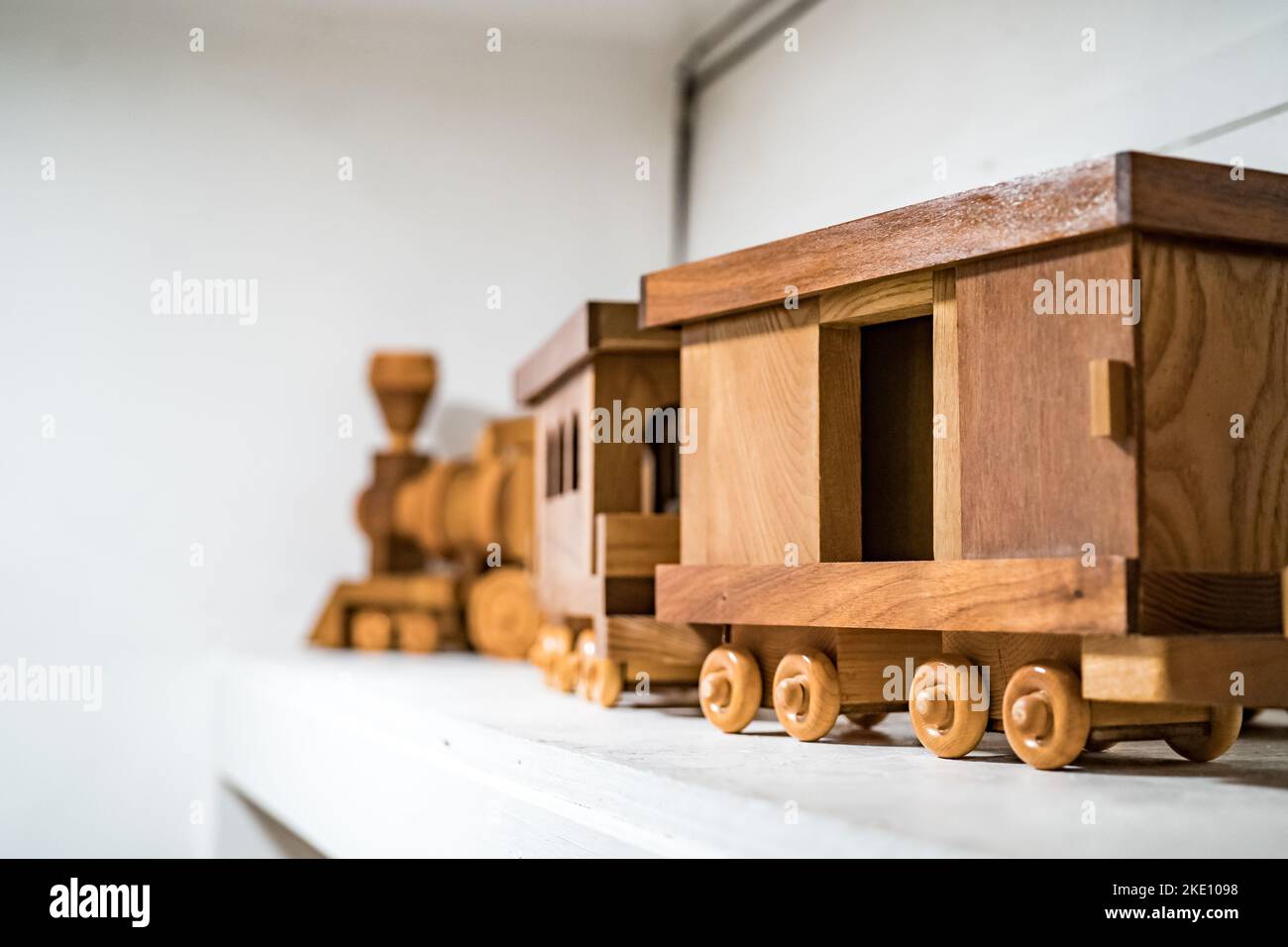 A closeup of a handmade wooden train with wagons on a white shelf
