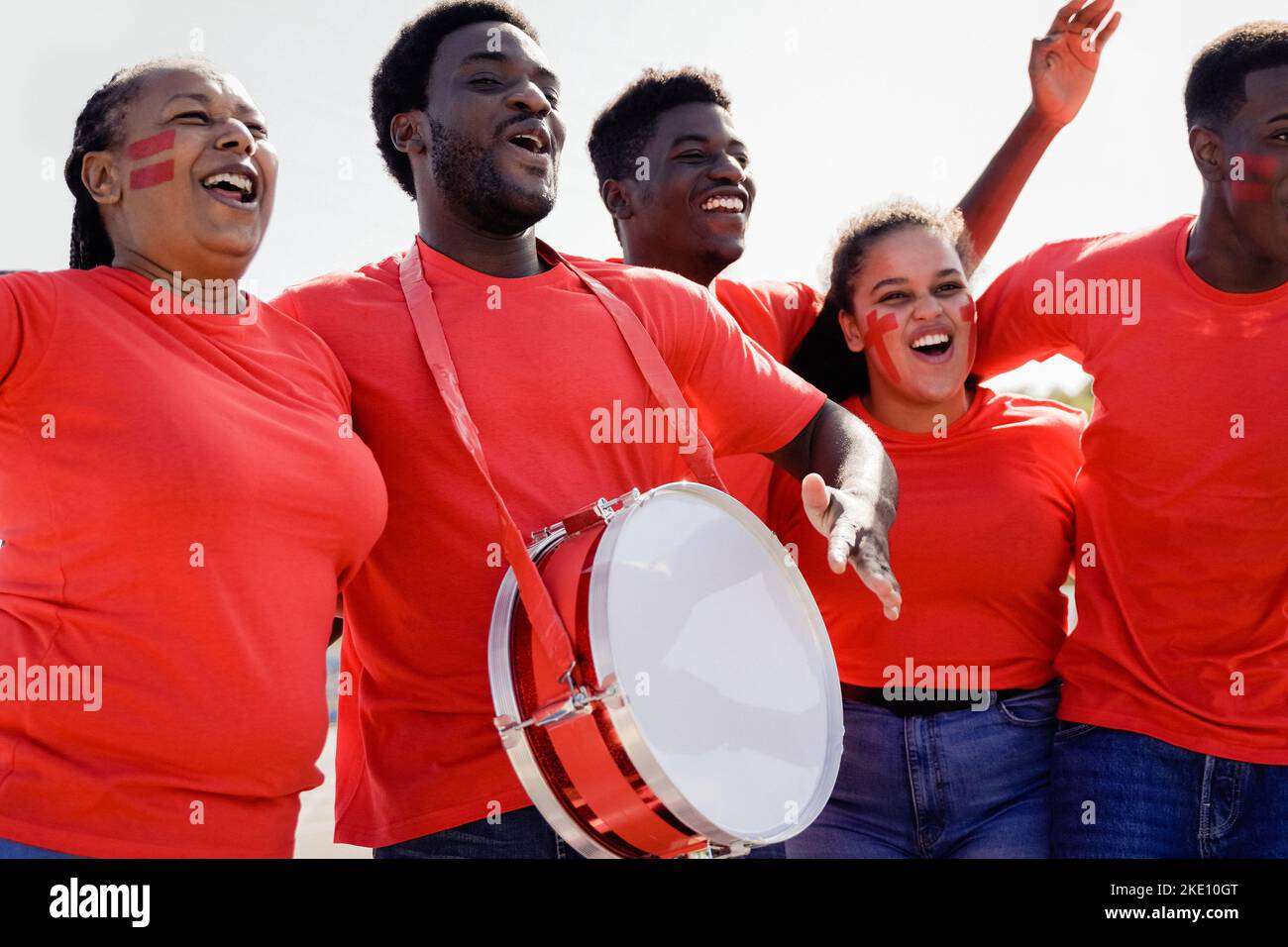 African red sport football fans celebrating team victory in championship game at stadium - Soccer supporters having fun in crowd - Focus on left man f Stock Photo