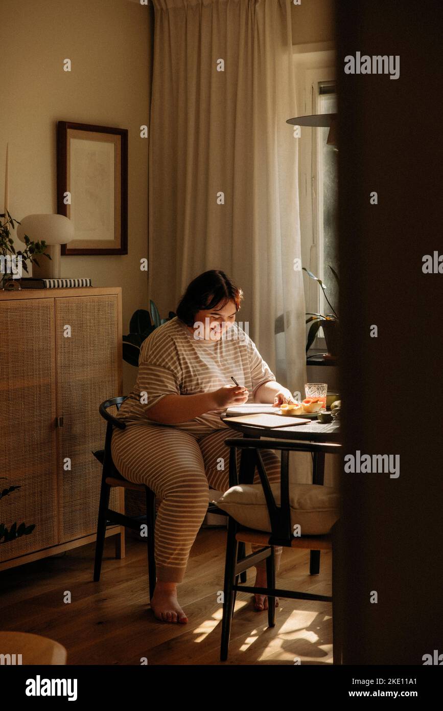 Smiling young woman writing while sitting at table Stock Photo
