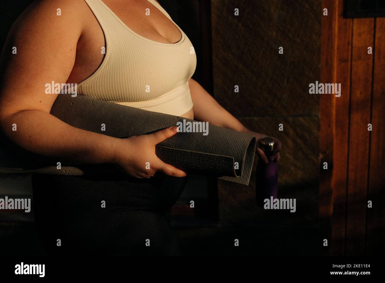 Midsection of young woman with exercise mat during sunset Stock Photo
