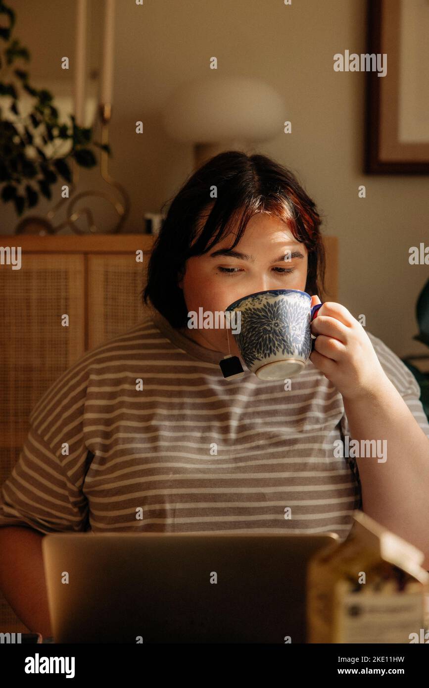 Young woman drinking coffee while using laptop at home Stock Photo