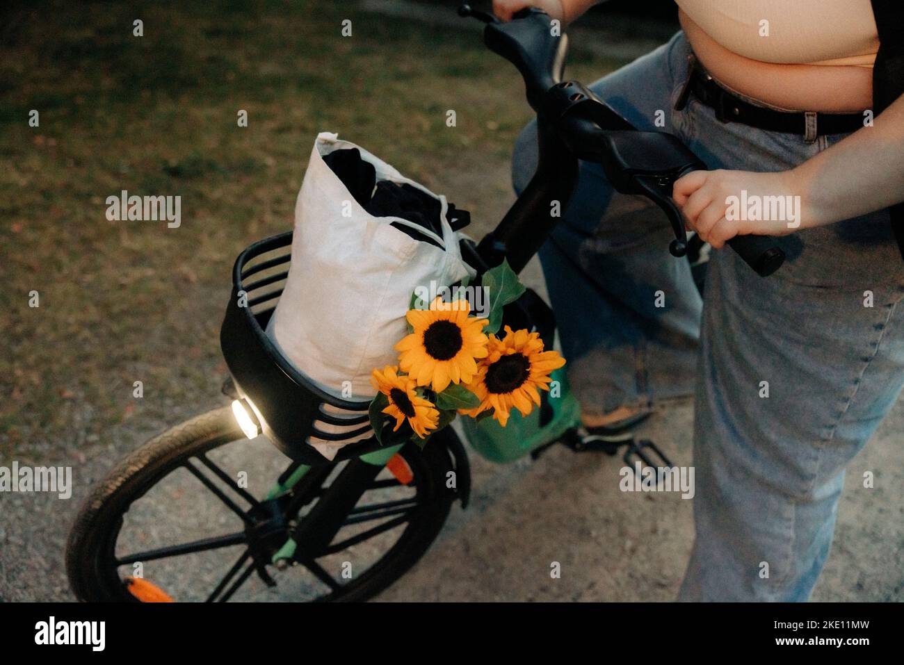 Low section of young woman by bicycle with reusable bag and sunflowers Stock Photo