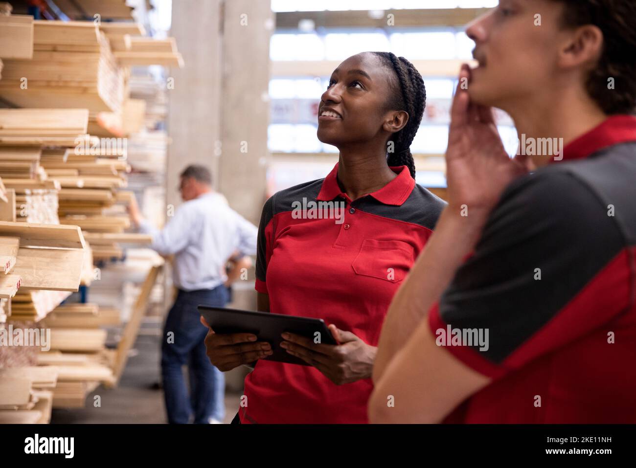 Saleswoman with digital tablet looking up while standing with male staff at hardware store Stock Photo