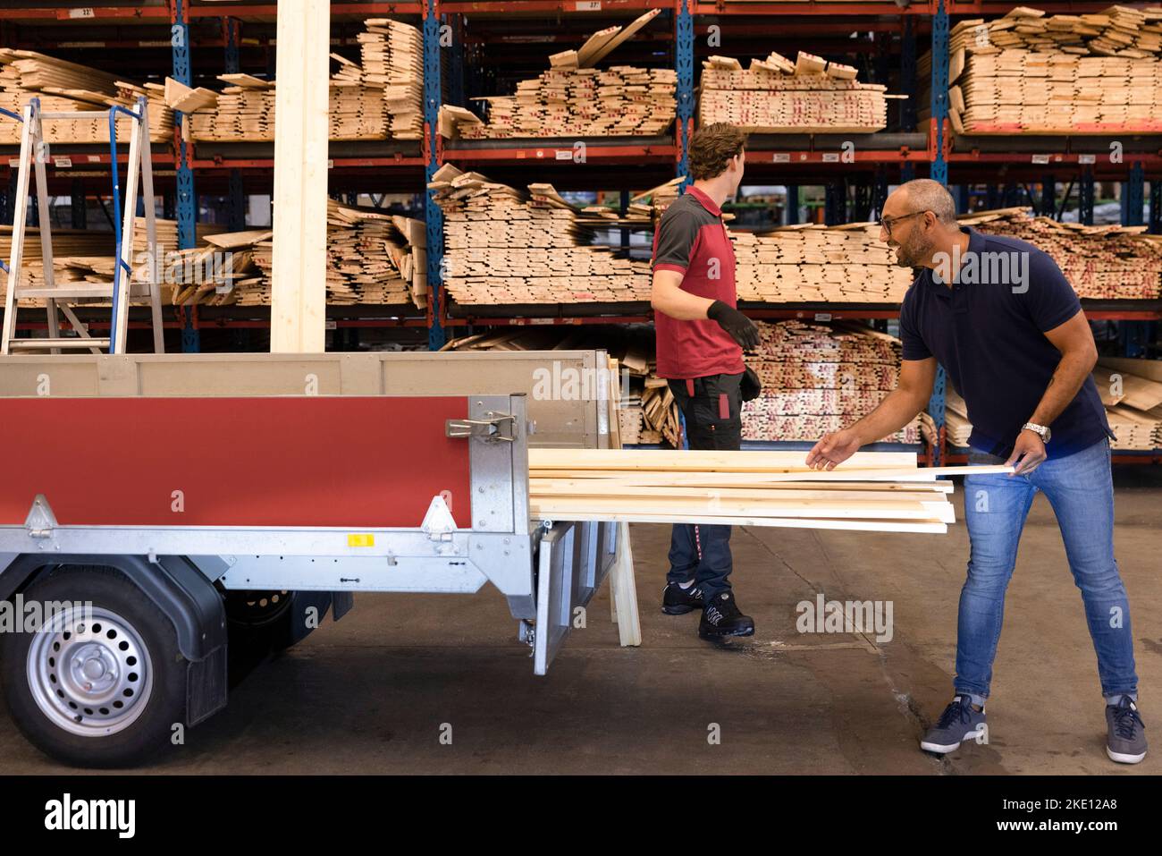 Mature man loading plank in vehicle trailer at hardware store Stock