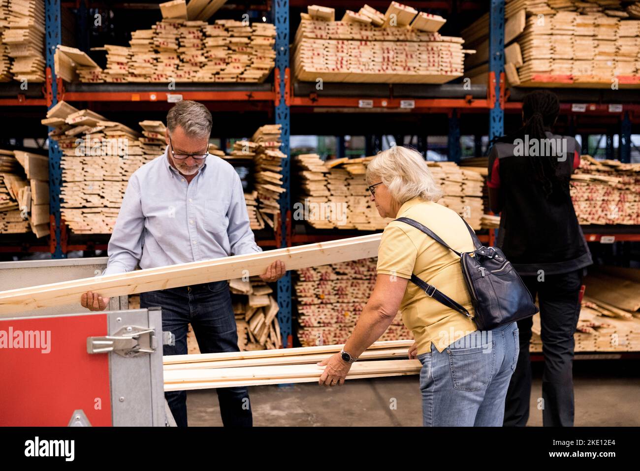 Senior customers examining and loading planks in trailer while shopping