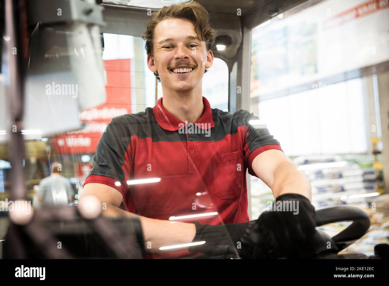 Portrait of happy male warehouse worker sitting in forklift seen through windshield Stock Photo