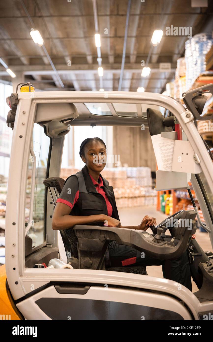 Side view of female warehouse worker sitting in forklift at warehouse Stock Photo