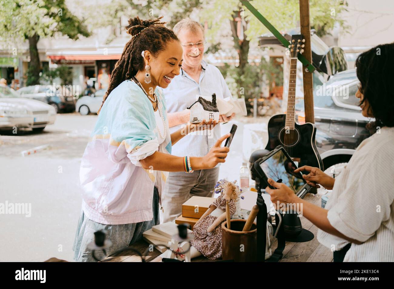 Happy female customer paying while holding house model near stall at flea market Stock Photo