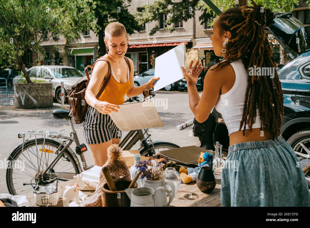 Female owner communicating with customer holding records while shopping at flea market Stock Photo