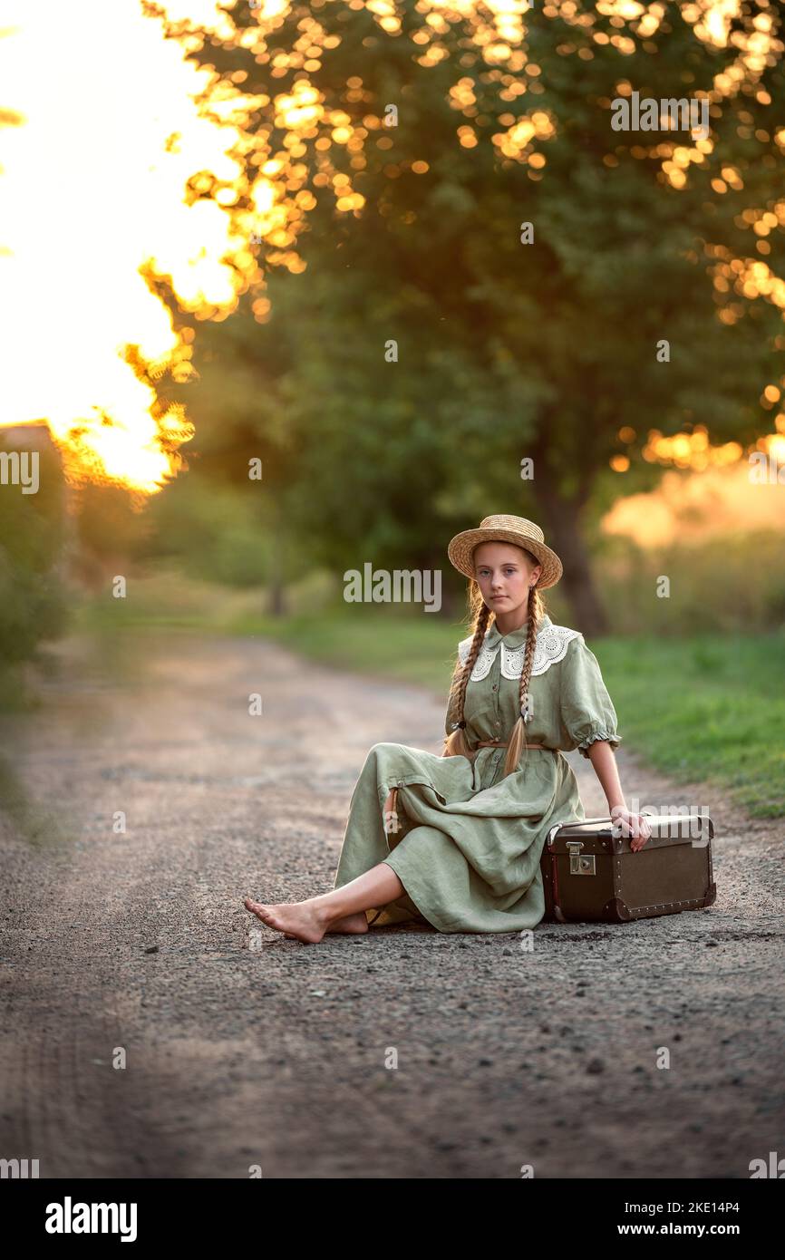 girl at sunset sits on the road in a hat and vintage dress Stock Photo