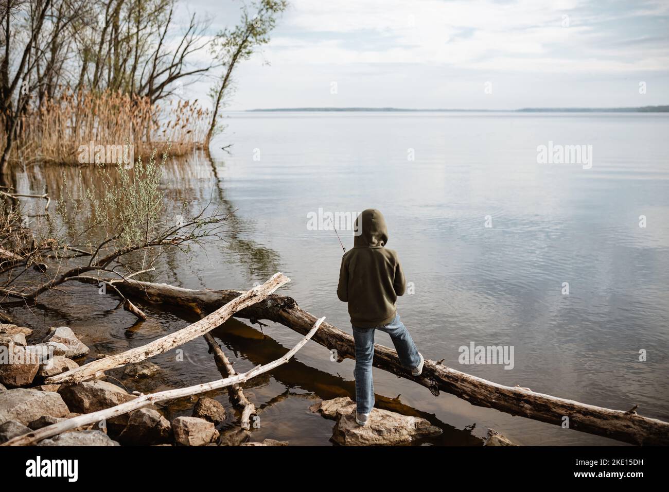 Young boy standing lakeside fishing during spring Stock Photo