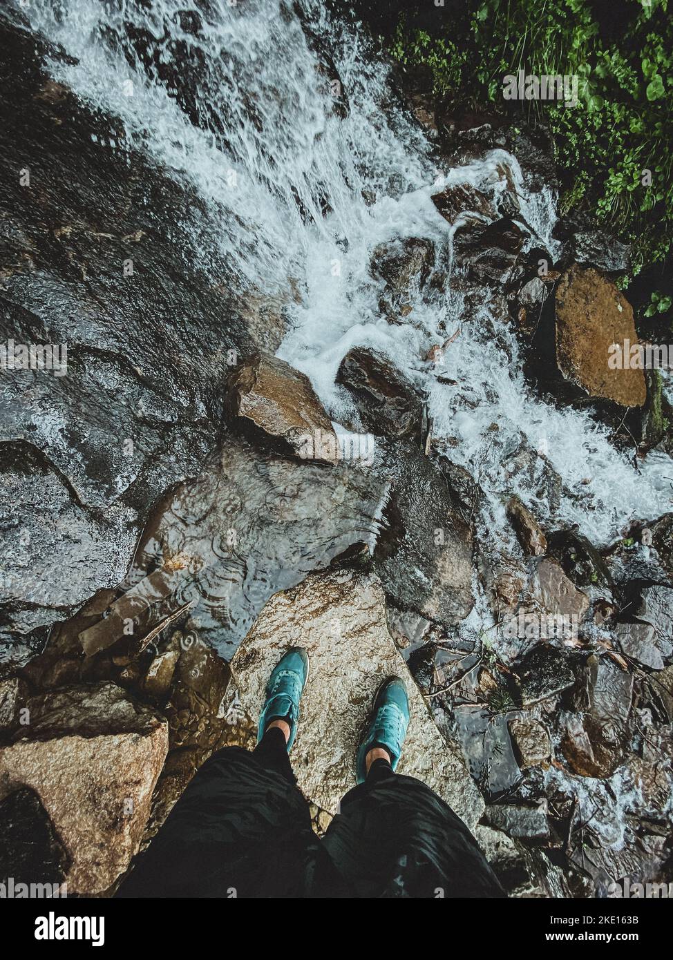 Legs from above standing on the rock near waterfall in mountains Stock Photo