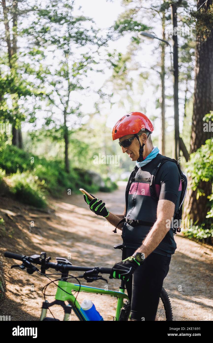Man using smart phone while standing with cycle on footpath Stock Photo