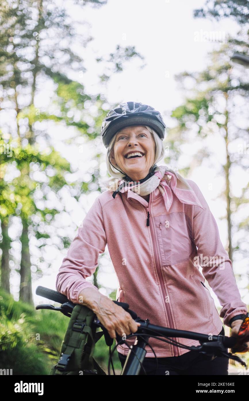 Smiling senior woman looking away while standing with cycle Stock Photo