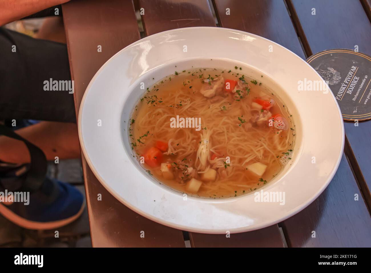 Bojnice, Slovakia - 06.11.2022: Soup with noodles and vegetables in a white plate on a wooden table. Stock Photo
