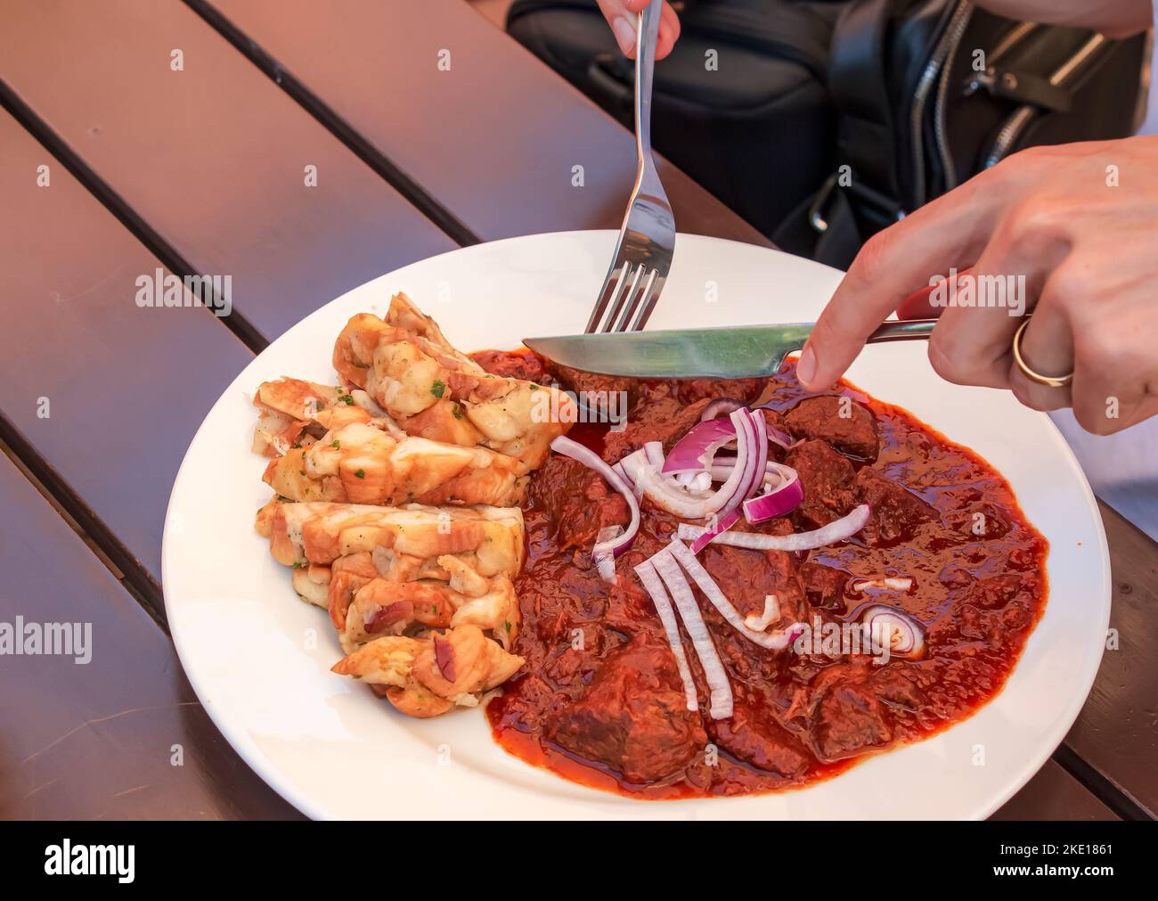 A man eats beef goulash with Czech dumplings with a knife and fork. Stock Photo
