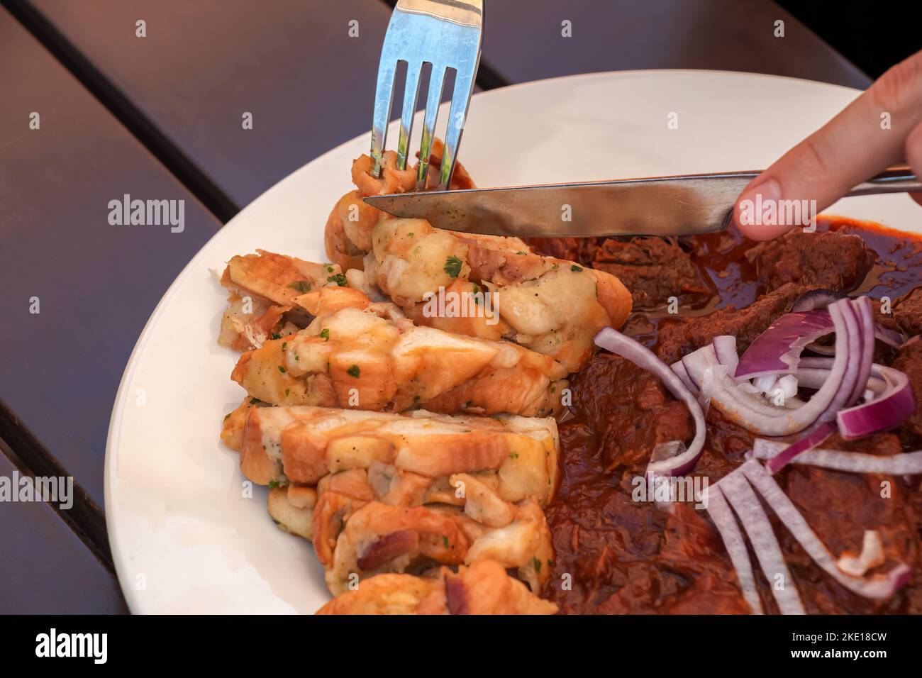 A man eats beef goulash with Czech dumplings with a knife and fork. Stock Photo