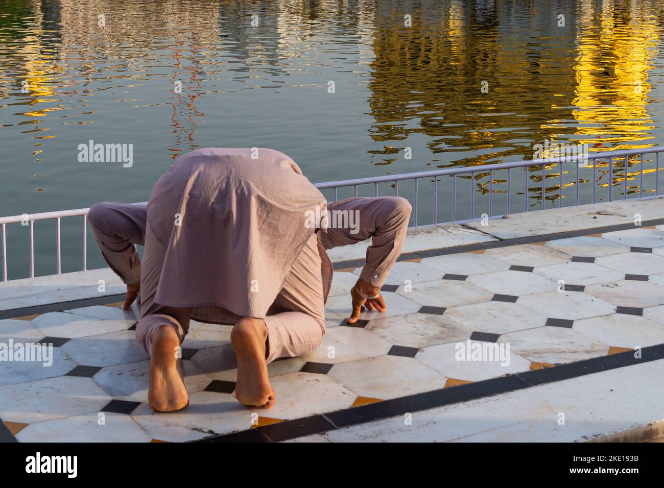 Man on his knees bowing to the Golden Temple in Amritsar India Stock Photo