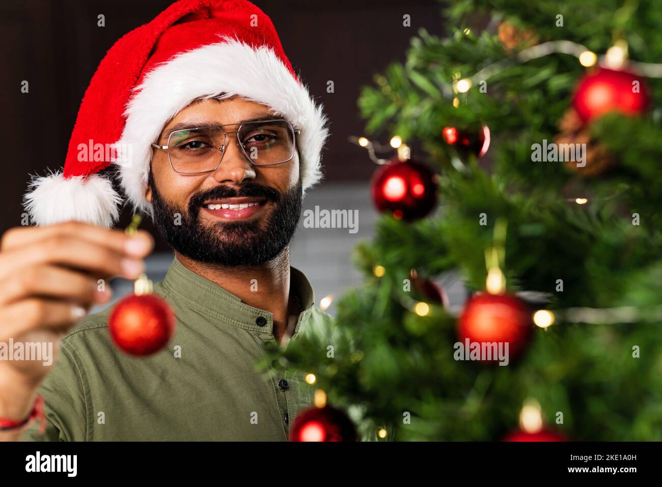 indian man in santa hat decorating Christmas tree with baubles Stock Photo