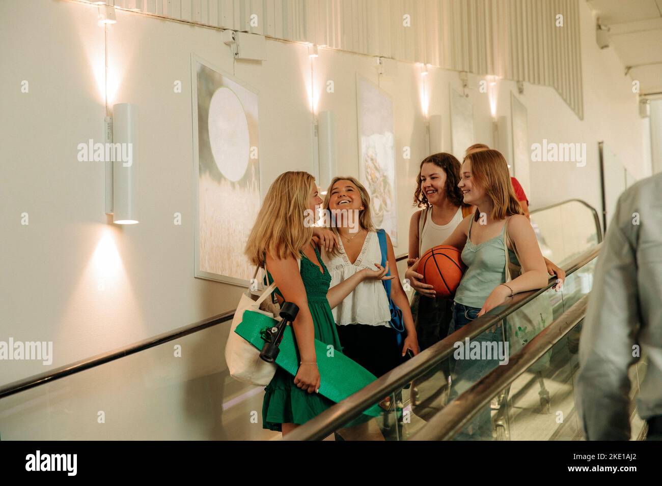 Happy teenage girls with basketball and skateboard on escalator in mall Stock Photo