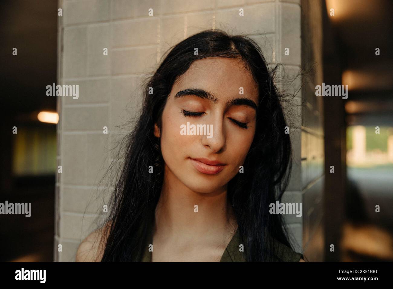 Teenage girl with eyes closed against column Stock Photo
