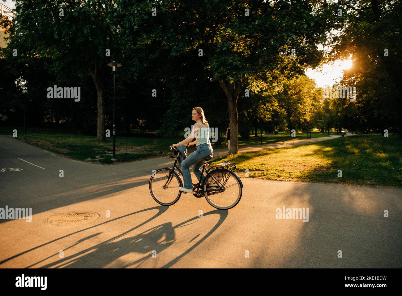 Side view of teenage girl riding bicycle on road at park during sunset Stock Photo