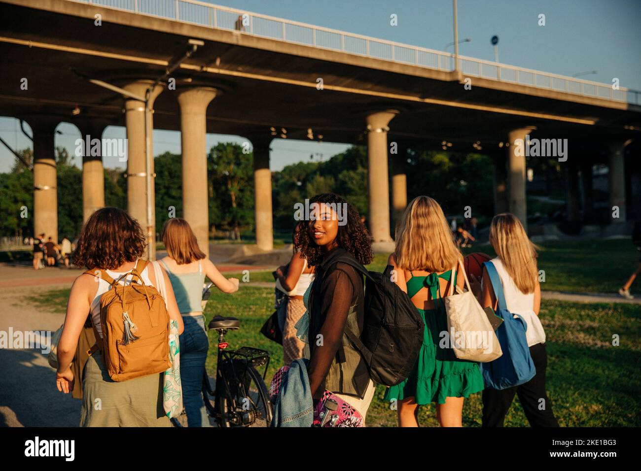 Portrait of smiling teenage girl walking with friends against bridge at park Stock Photo