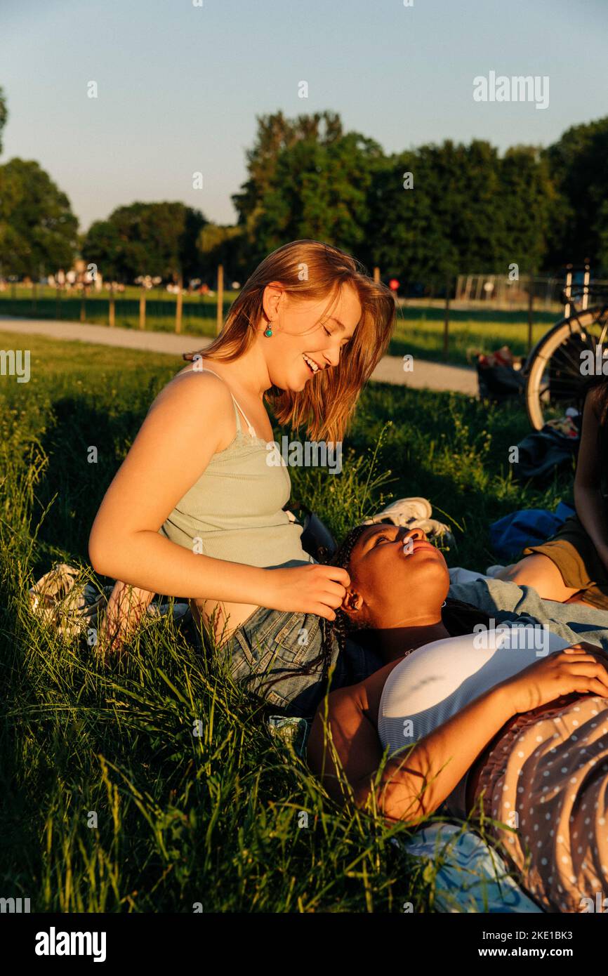 Smiling teenage girl talking with female friend lying on lap at park Stock Photo