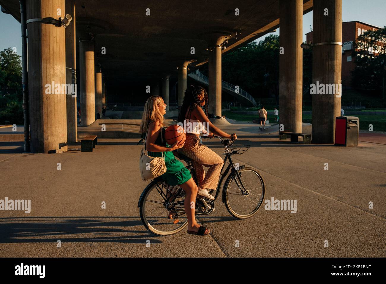 Side view of teenage girl sitting with friend riding bicycle on road during sunny day Stock Photo