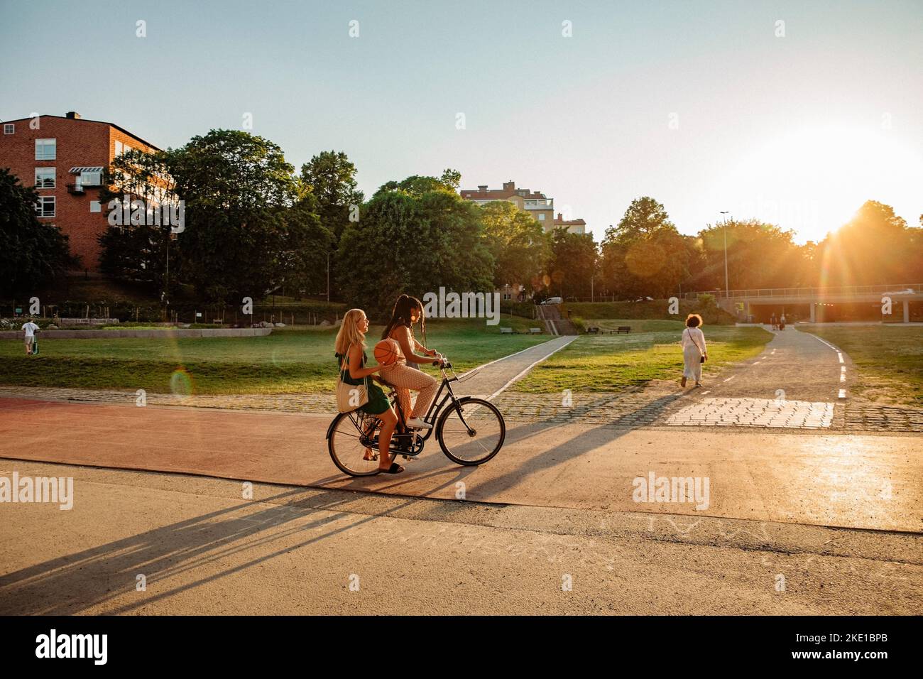 Teenage girl sitting with friend riding bicycle at park during sunset Stock Photo