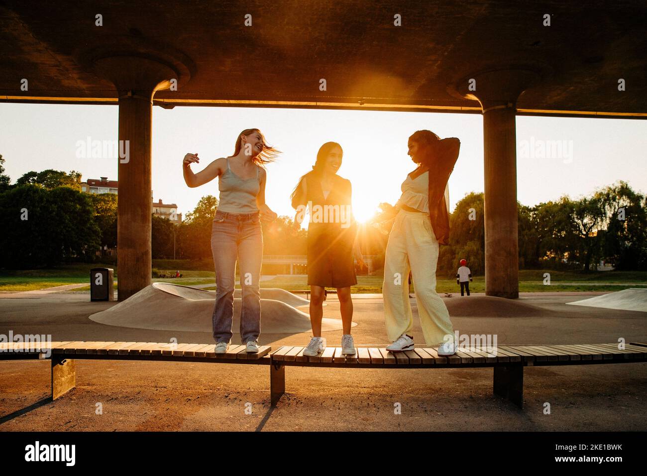 Happy teenage girl dancing on bench while enjoying under bridge during sunset Stock Photo