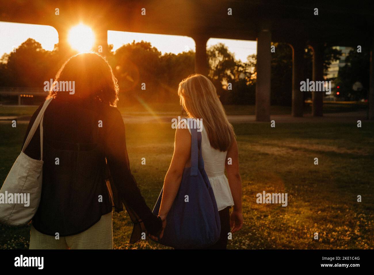 Teenage girls holding hands while walking at park during sunset Stock Photo