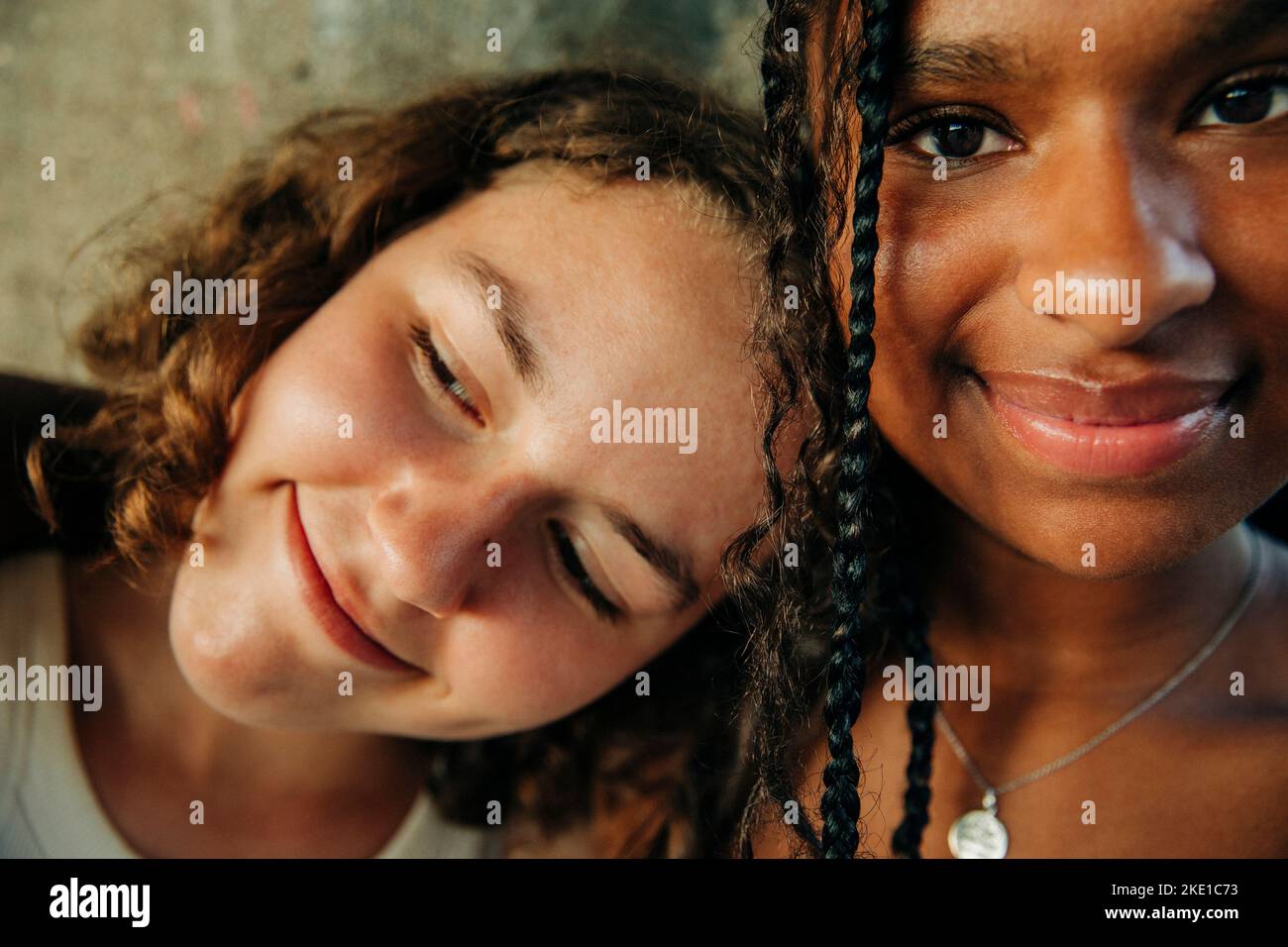 Thoughtful smiling teenage girl leaning head on female friend Stock Photo