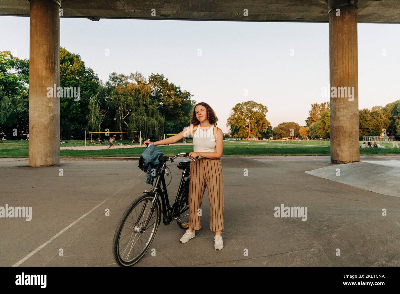 Teenage girl with bicycle standing in front of bridge at park Stock Photo
