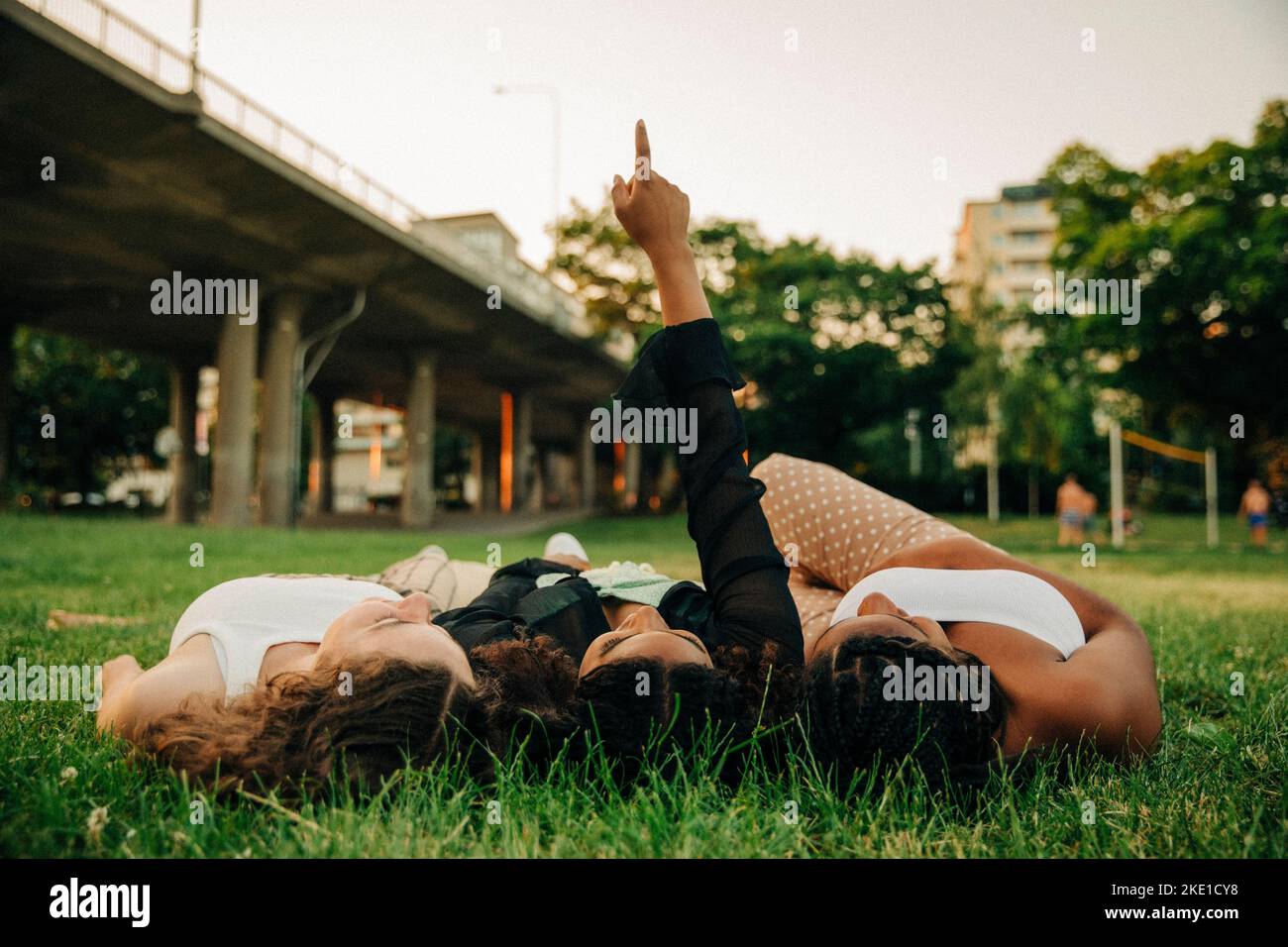 Teenage girl with hand raised pointing while lying amidst friends on grass at park Stock Photo