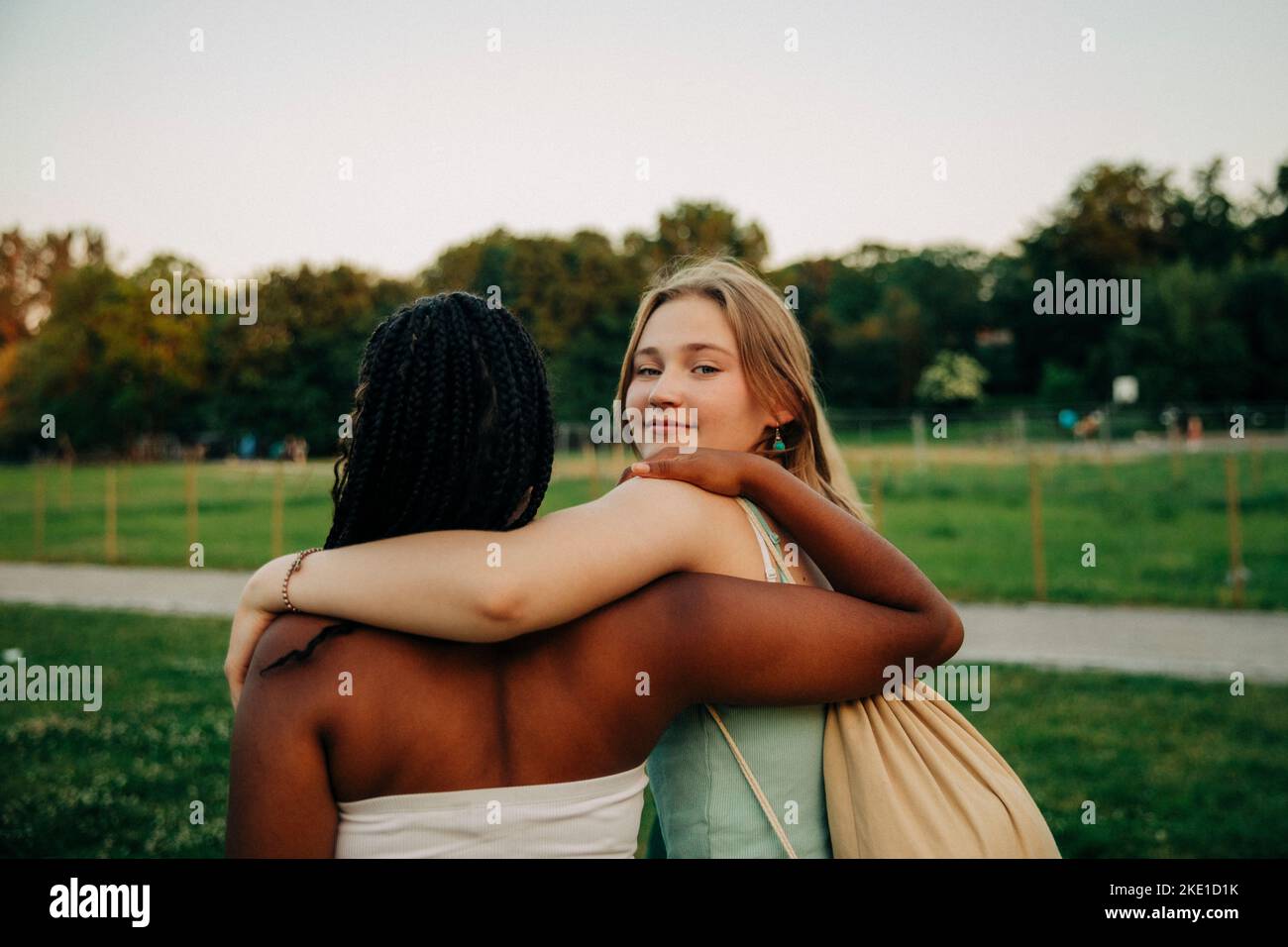Portrait of smiling teenage girl with arm around friend walking at park Stock Photo