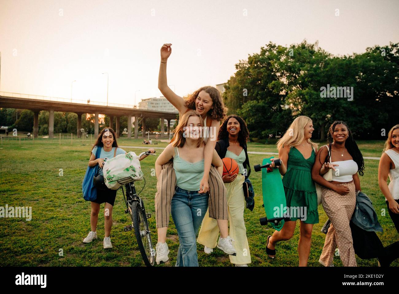 Happy teenage girl giving piggyback ride to female friend at park Stock Photo