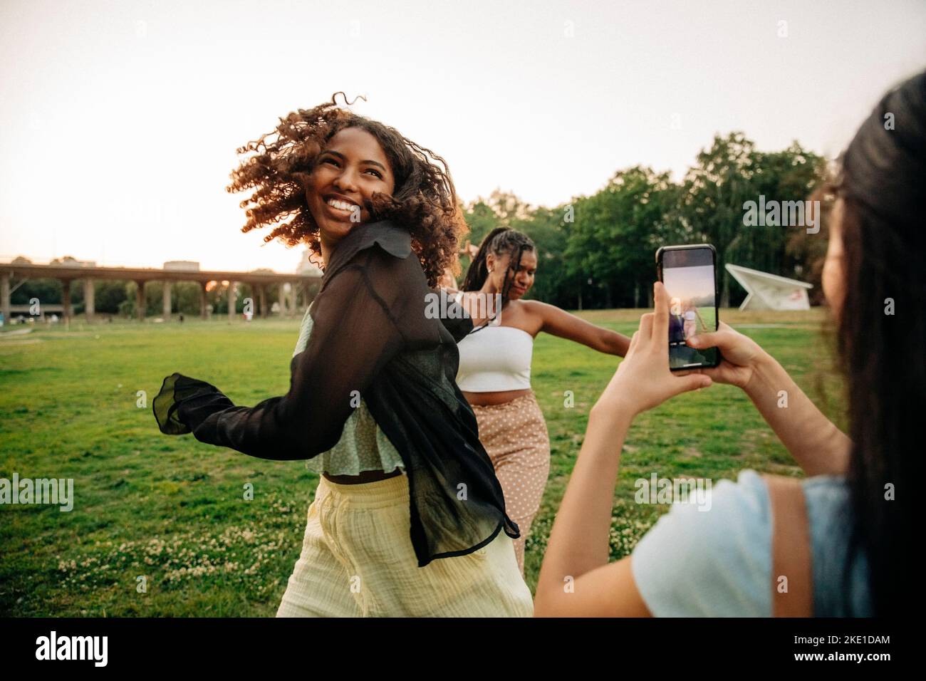 Teenage girl photographing happy female friends dancing in park Stock Photo