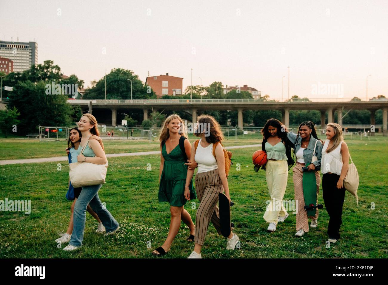 Smiling teenage girls talking with each other while walking in park at sunset Stock Photo