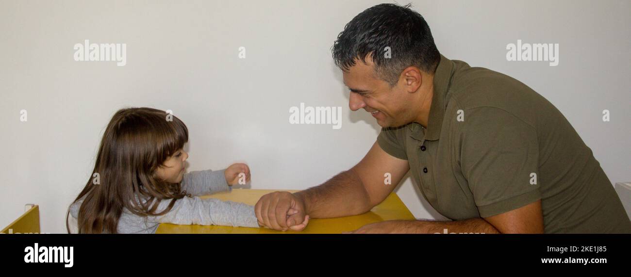Image of a young dad playing arm wrestling with his daughter. You play at home and the dad wins a showdown Stock Photo